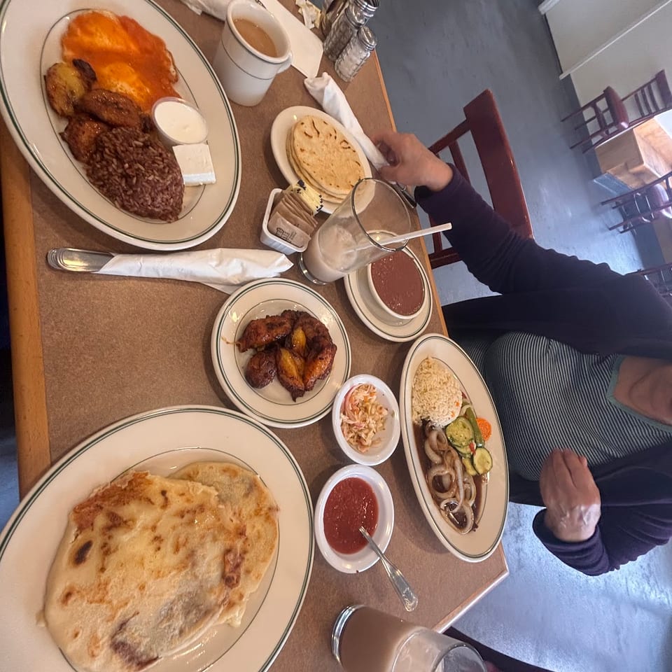 Restaurant table filled with Mexican dishes, including rice, beans, enchiladas, tortillas, salsa, roasted vegetables, drinks, and diners.