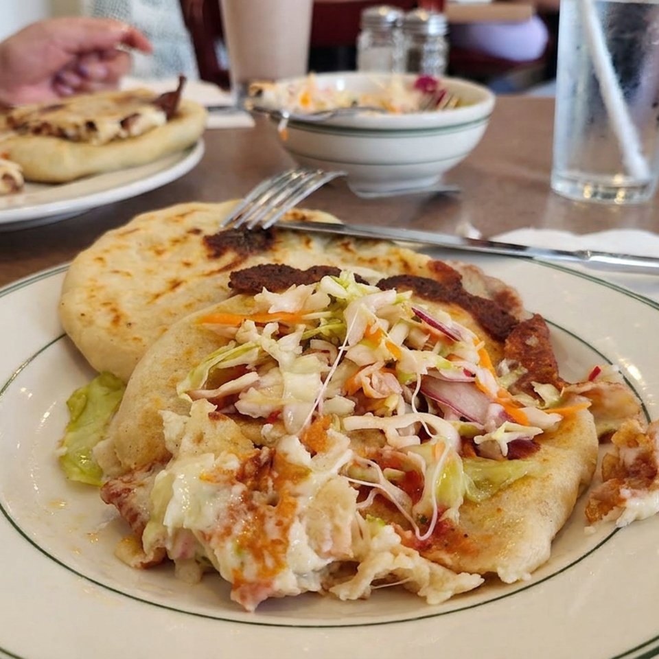 Plate of stuffed flatbreads topped with shredded vegetables and sauce, with diners, water glasses, and another plate in the restaurant.